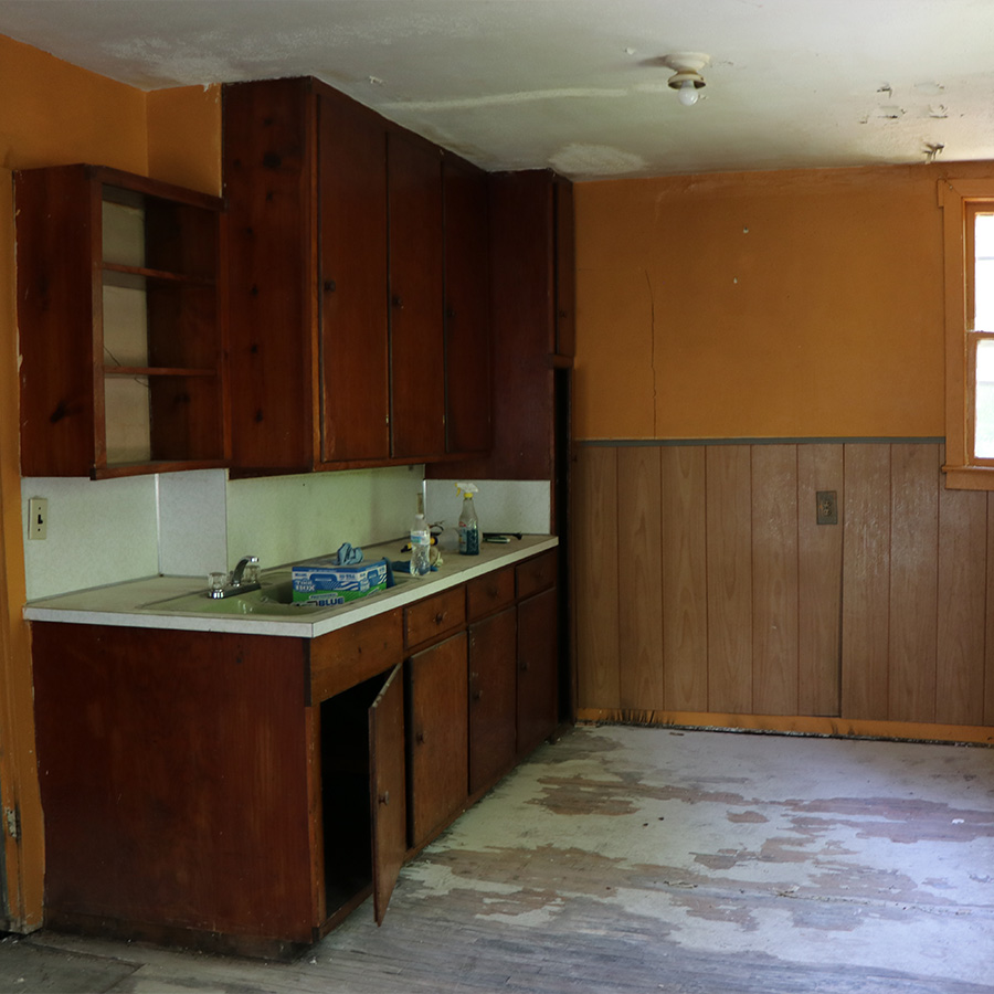 Dated kitchen with dark wood cabinets, orange walls and damaged flooring
