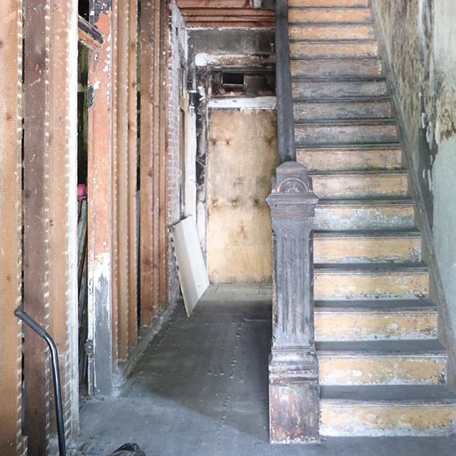 Gutted hallway with exposed studs, brick and a stripped staircase