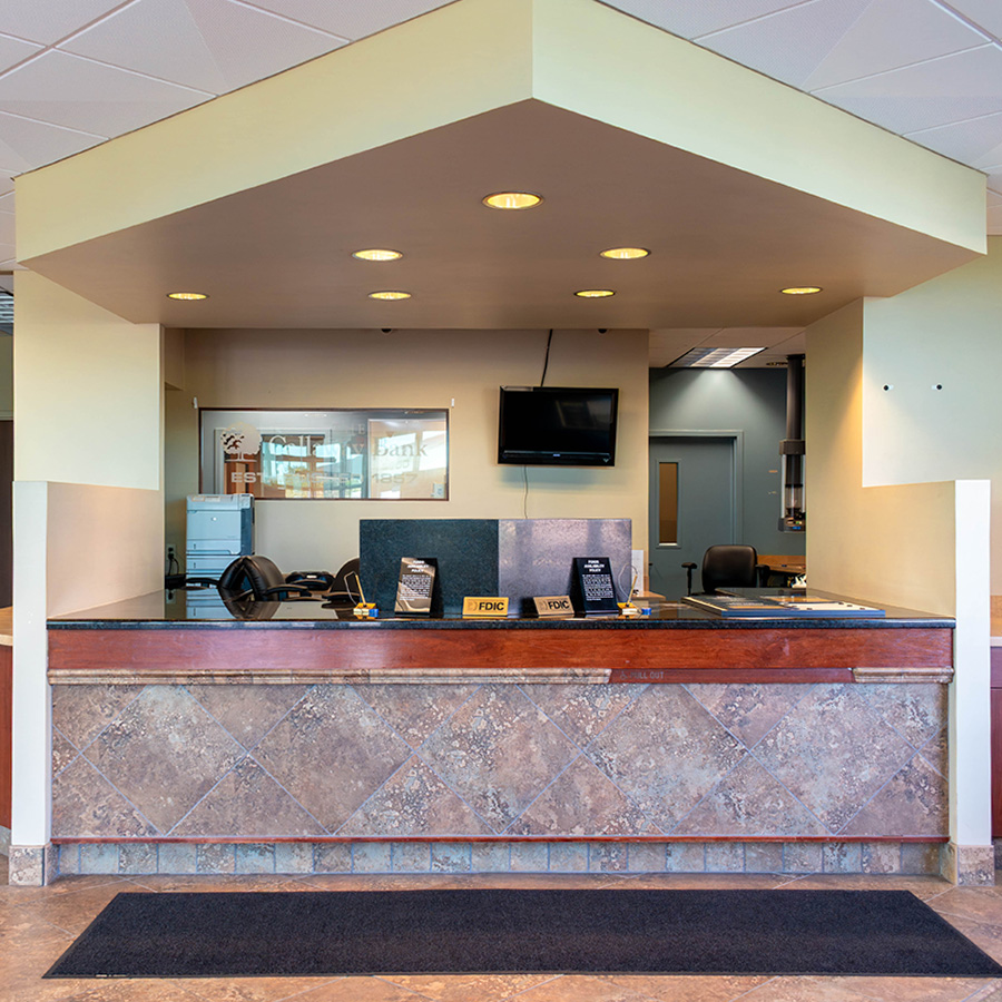 Bank teller line with tan and sage walls and warm dated lighting