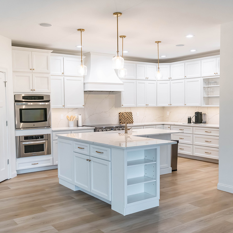 Remodeled white kitchen with quartz island, marble-look backsplash and brass pendants