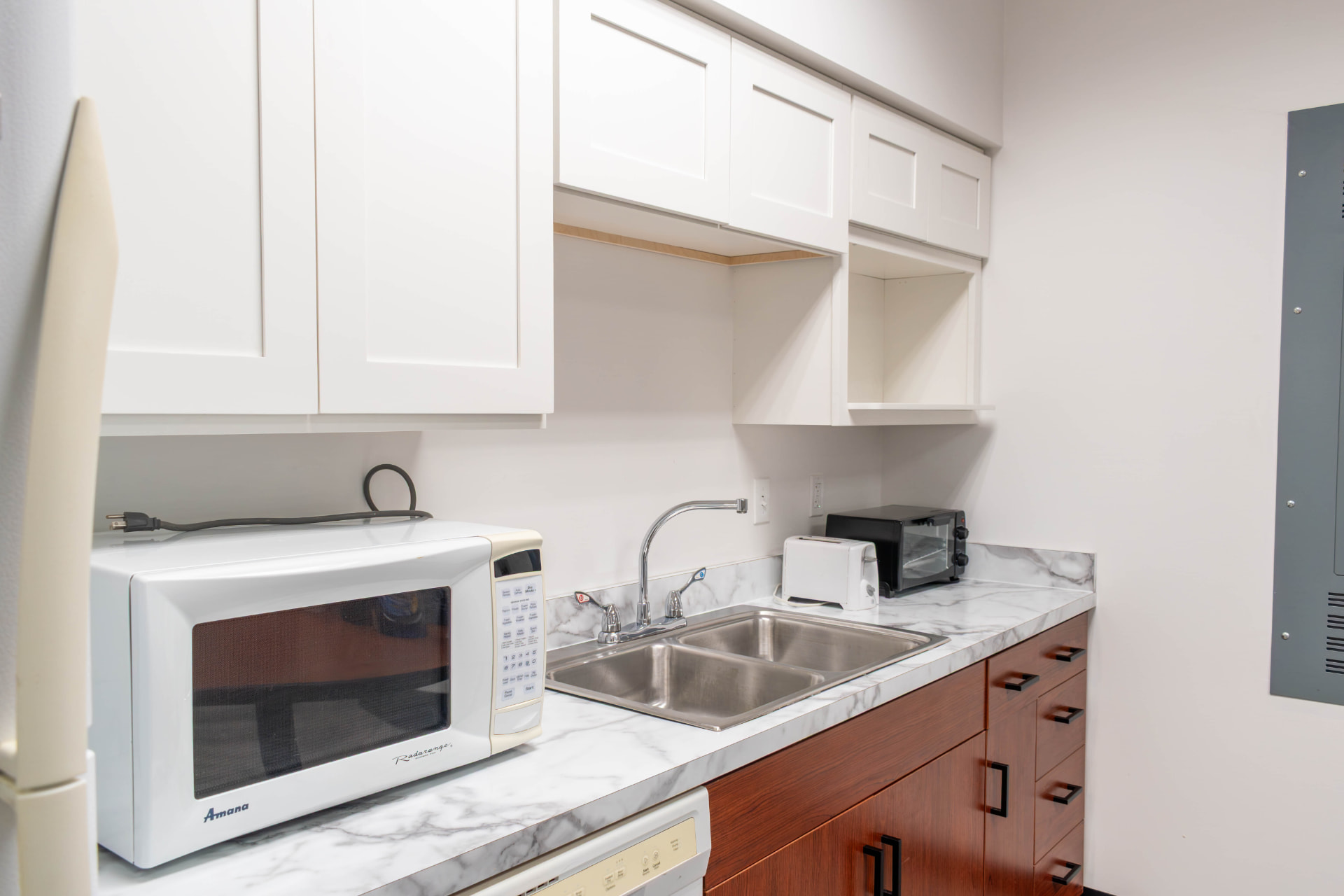 Break room kitchenette with white shaker upper cabinets, marble-look counters and white walls