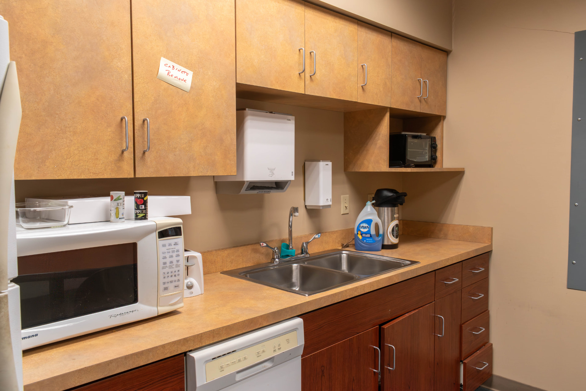 Break room kitchenette with tan laminate upper cabinets, beige counters and beige walls