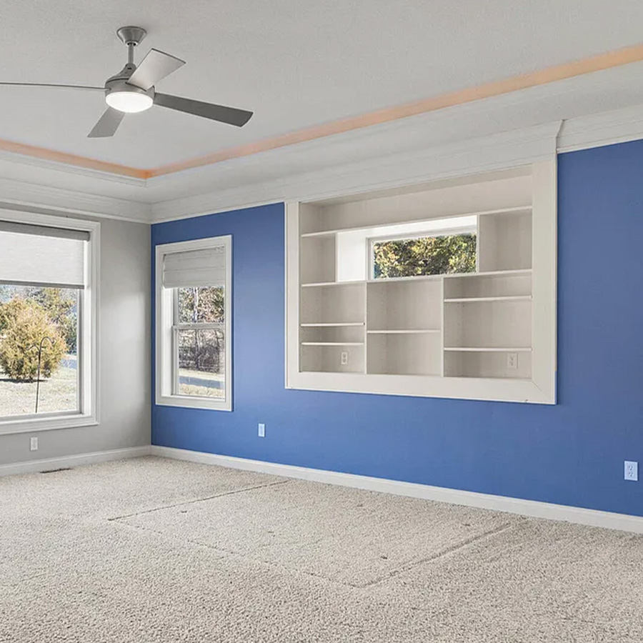 Empty bedroom with blue accent walls, white built-in shelving and beige carpet