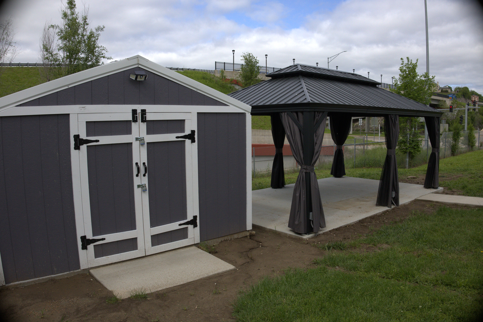 Backyard gazebo with a black metal roof and curtains beside a matching storage shed
