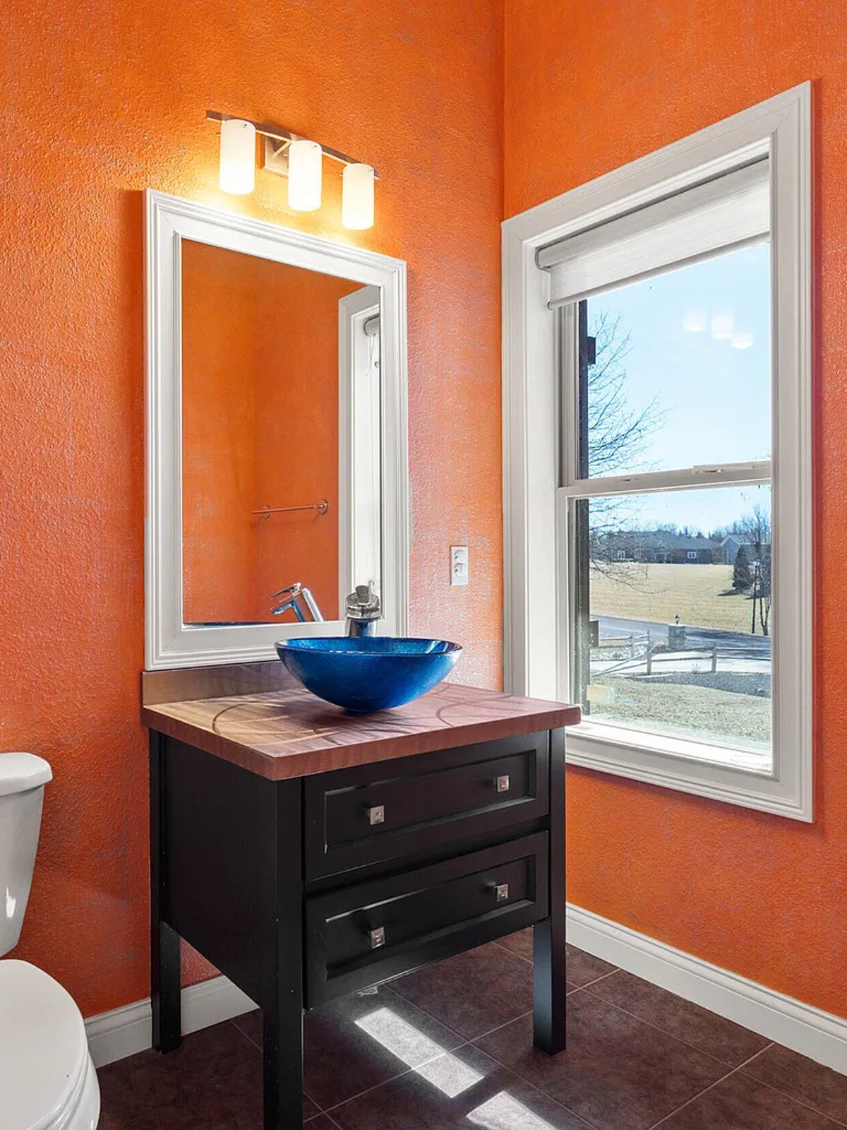 Powder room with orange textured walls, a blue glass vessel sink and dark tile floor