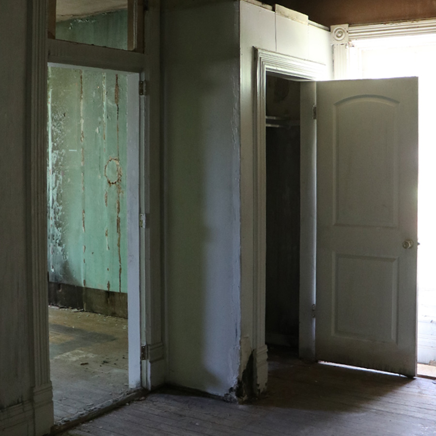 Dim bedroom with damaged walls, old doors and worn flooring
