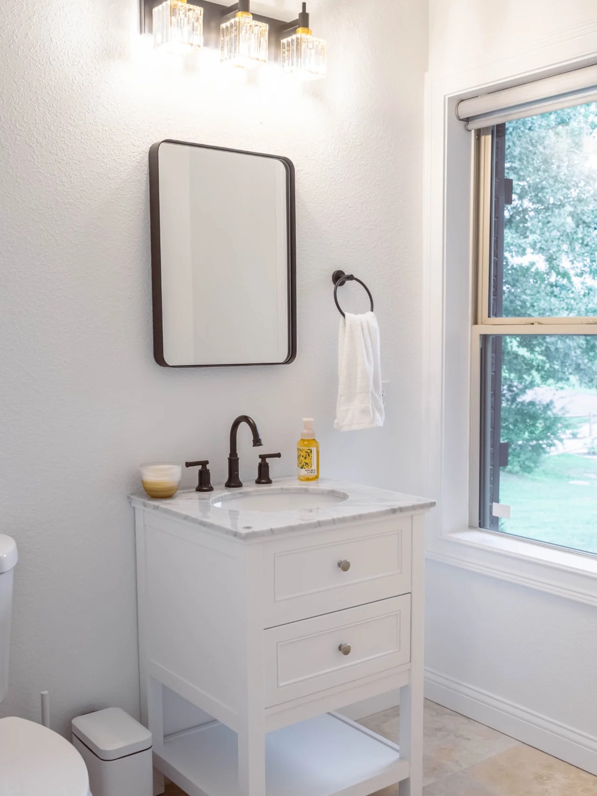 Powder room with white walls, a marble-top vanity, bronze fixtures and light stone floor
