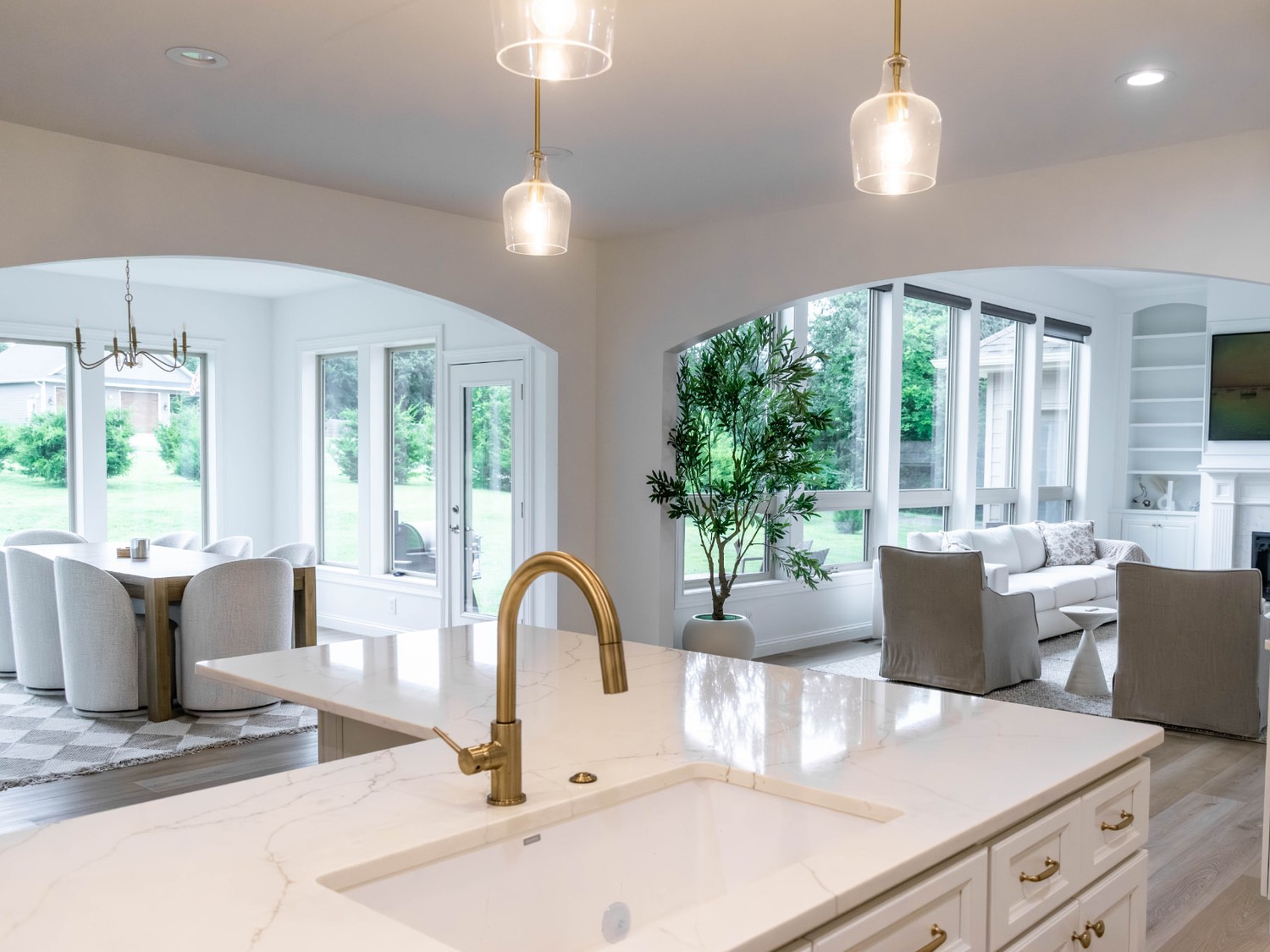 Open kitchen with white quartz island, brass faucet and glass pendants looking into the living room